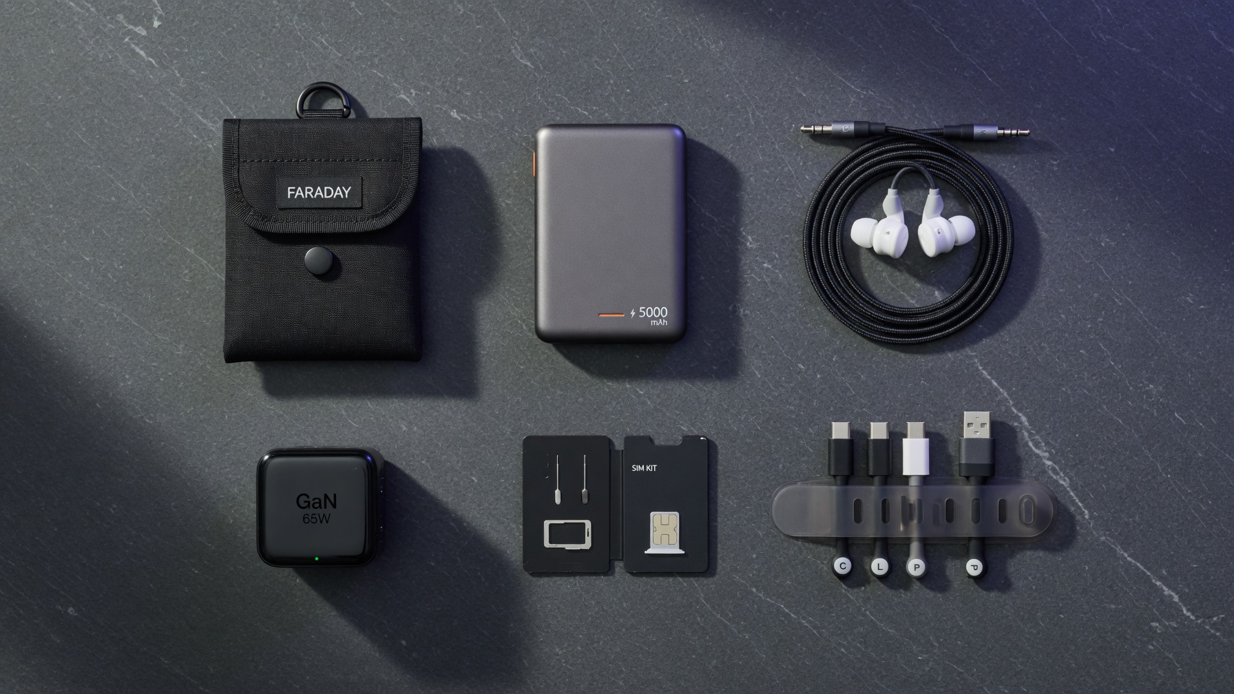 Complete dumbphone accessories collection flat lay: Faraday bag, power bank, wired headphones, GaN charger, SIM tools, cable organizer on dark slate
