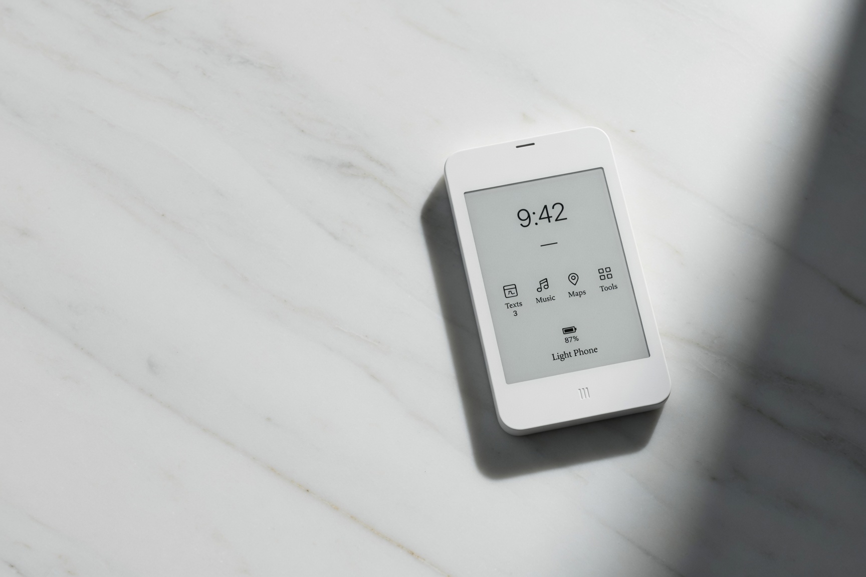 Light Phone III matte white phone on white marble showing e-ink dashboard with Texts, Music, Maps, Tools