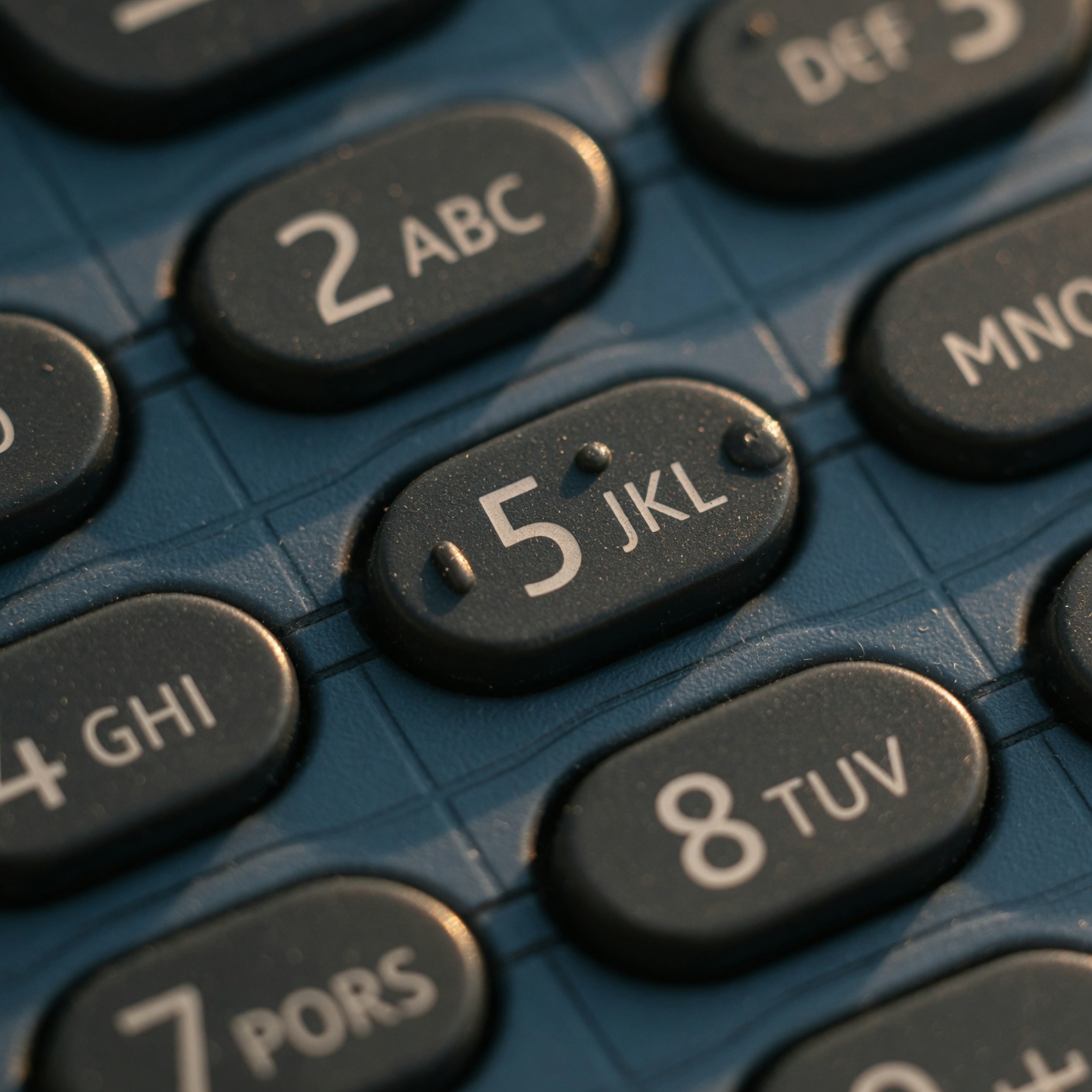 Nokia 3210 T9 numeric keypad macro — raised circular keys with number and letter engravings, warm side light