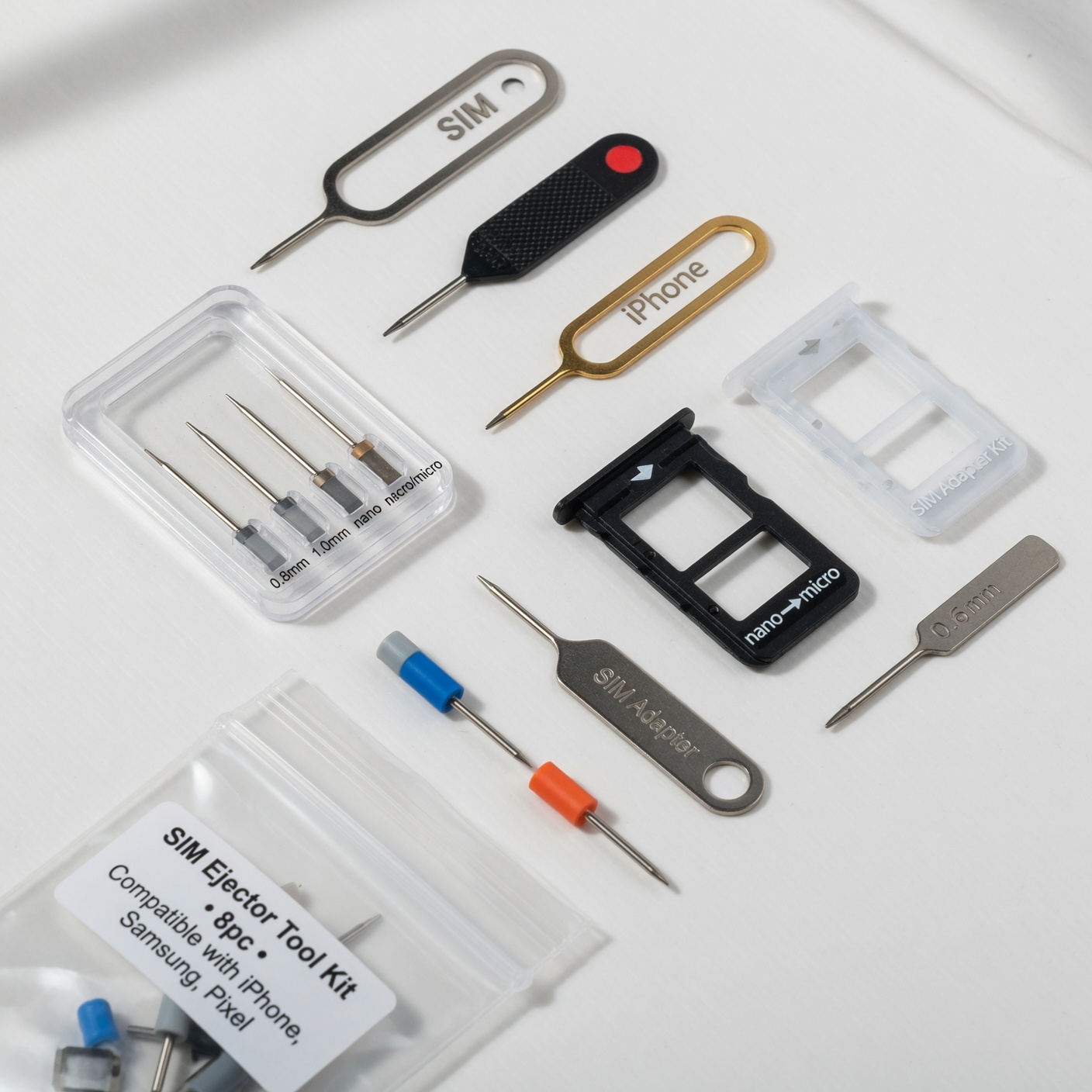 SIM card ejector tool kit with metal pin tools and SIM tray adapters on white surface